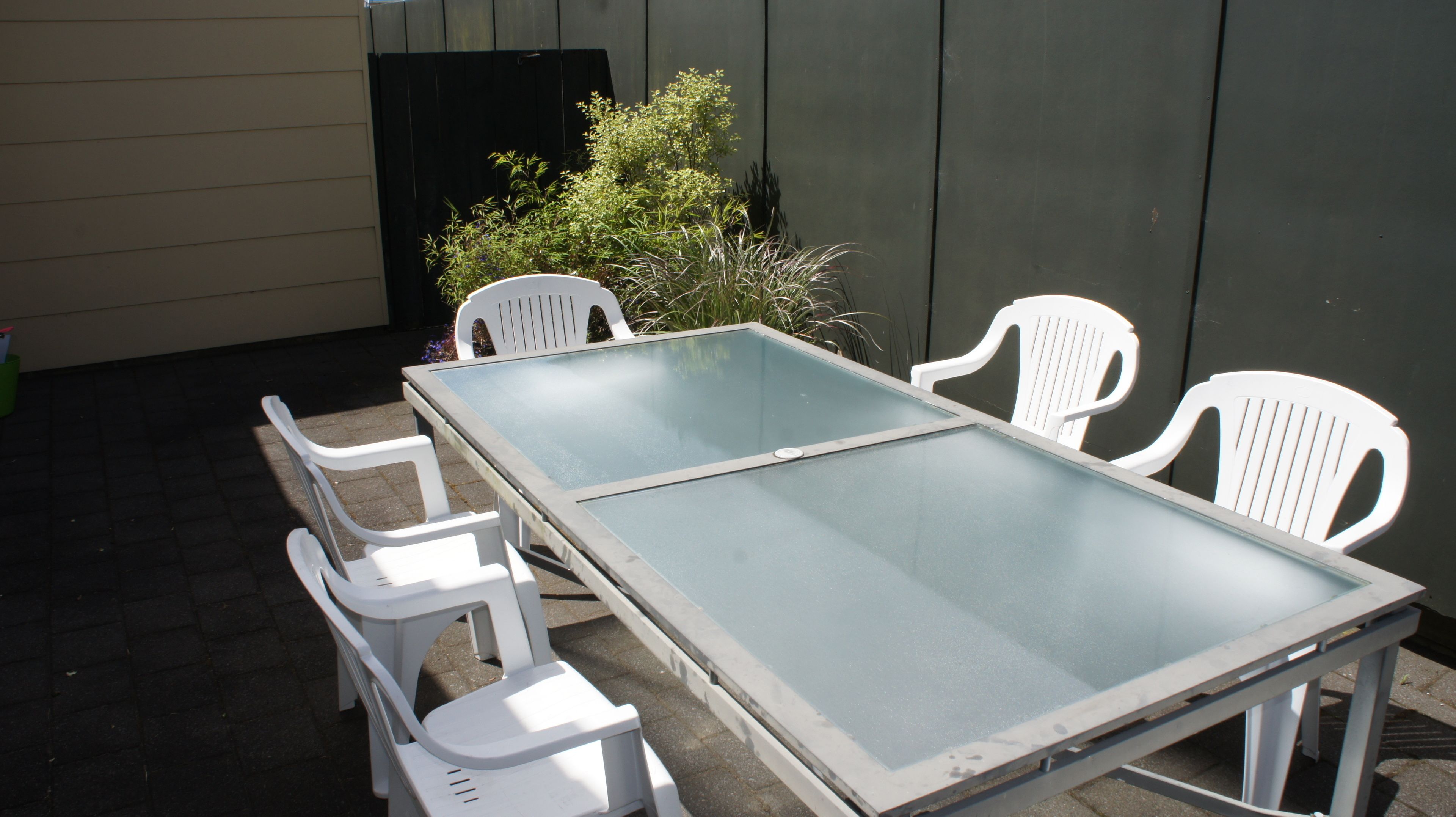 A table with a glass top and four white plastic chairs.