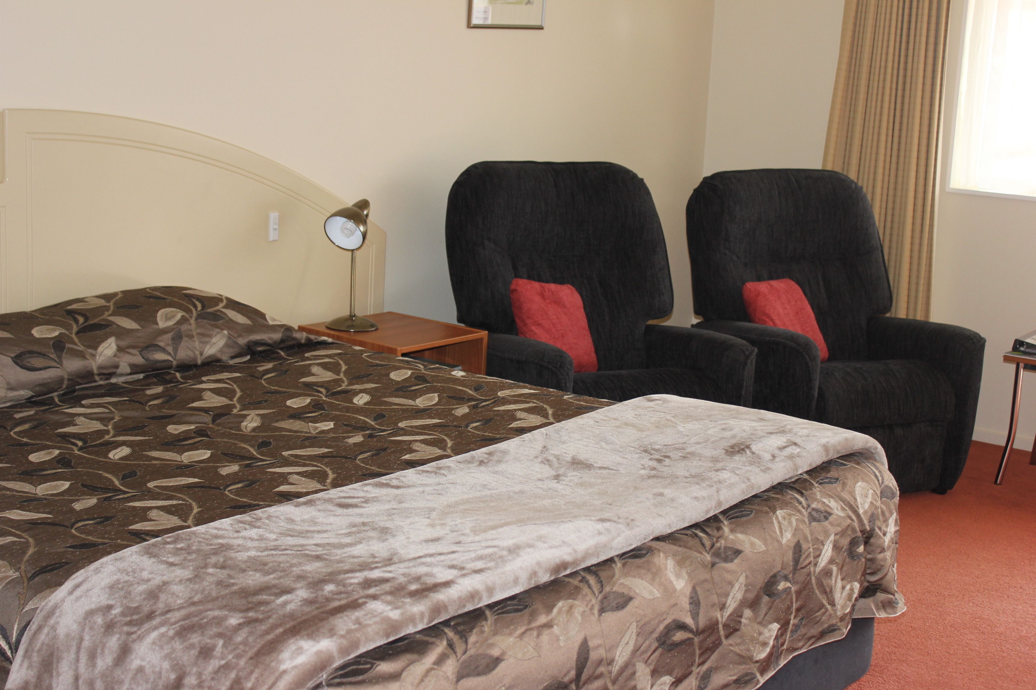A hotel room with a bed, two armchairs, a nightstand, and a lamp.