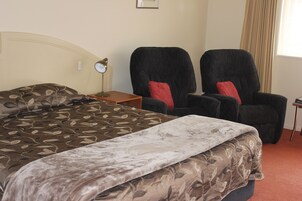 Una habitación de hotel con una cama, dos sillones, una mesita de noche y una lámpara.