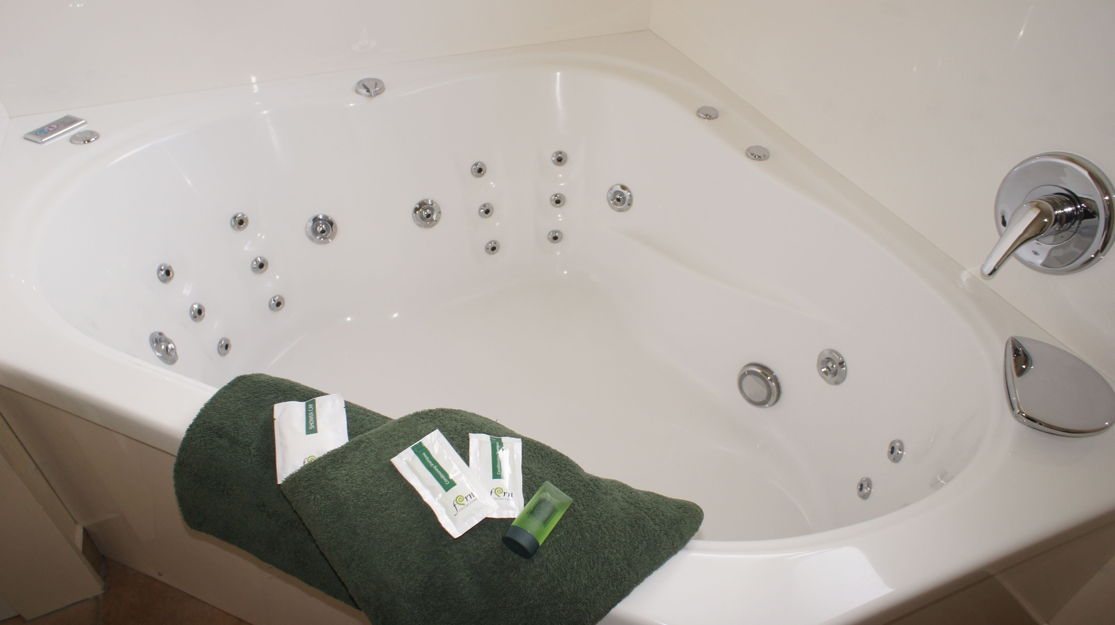 A white bathtub with multiple faucets, a showerhead, and a drain. There are two green towels with product labels on them.