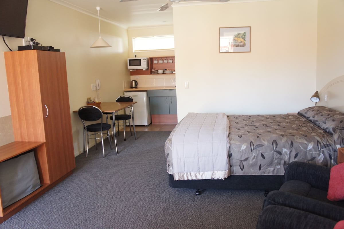 Ein kleines Zimmer mit Bett, Schreibtisch und Küchenzeile.