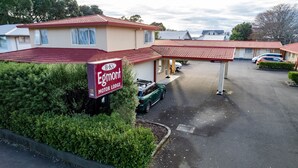A motor lodge with a red-tiled roof, a signboard, and a parking area with a green car.