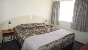 A bedroom with a bed, two bedside tables, a lamp, and a window with curtains.