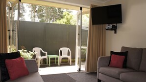 A living room with a grey sofa, a red pillow, and a television mounted on the wall.