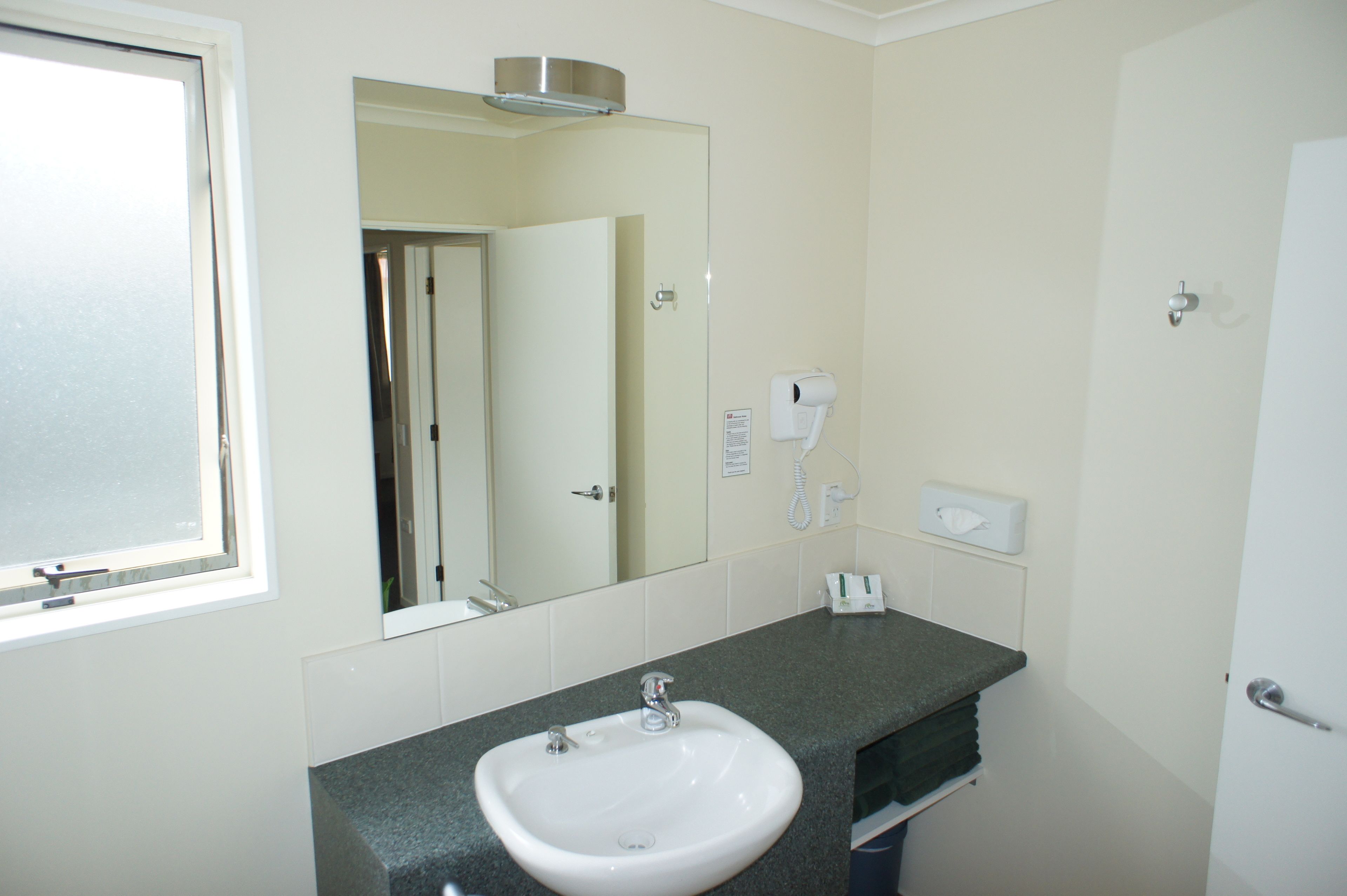 A bathroom with a white sink, a mirror, a hairdryer, and a phone.