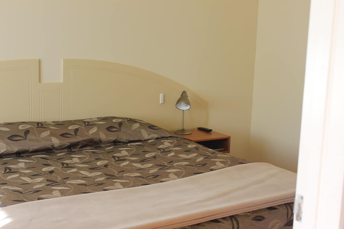 Ein Bett mit gemustertem Überwurf, eine Nachttischlampe und ein Nachttisch.