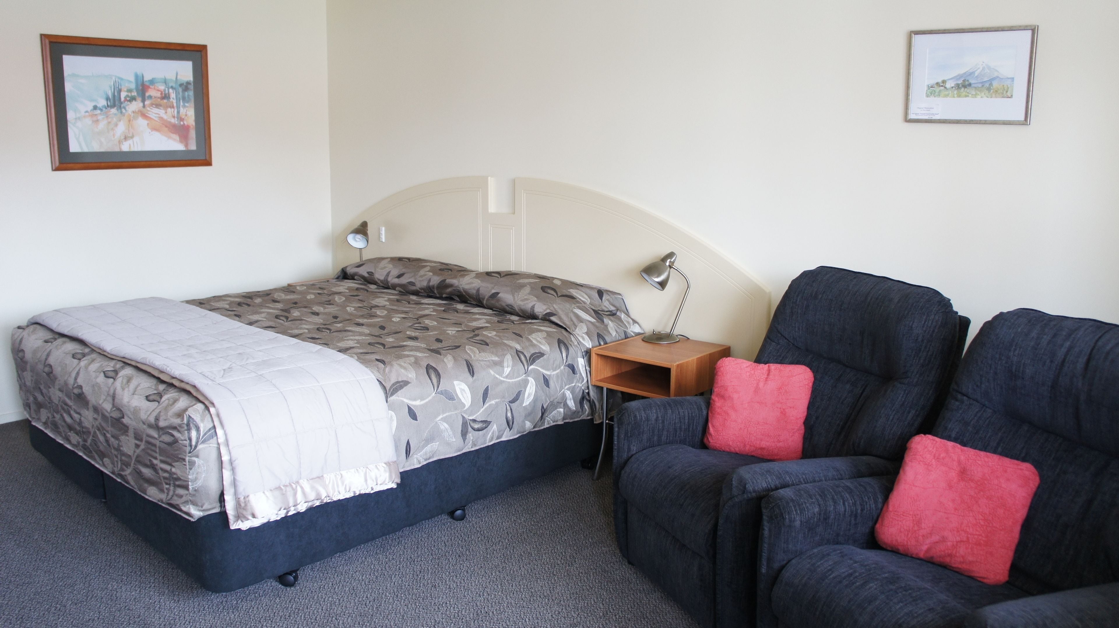 A bedroom with a bed, a nightstand, a lamp, and two chairs.