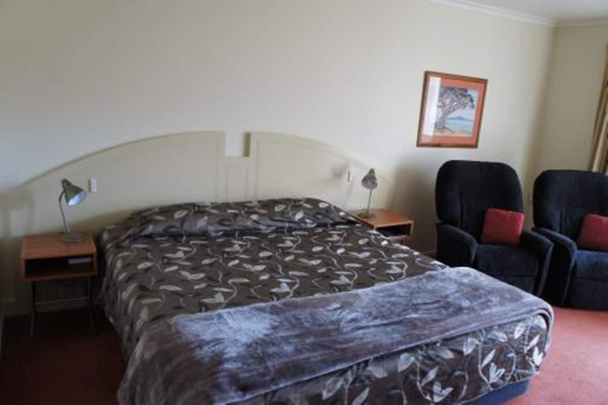 Ein Hotelzimmer mit Bett, Stuhl, Nachttisch und einem gerahmten Bild an der Wand.