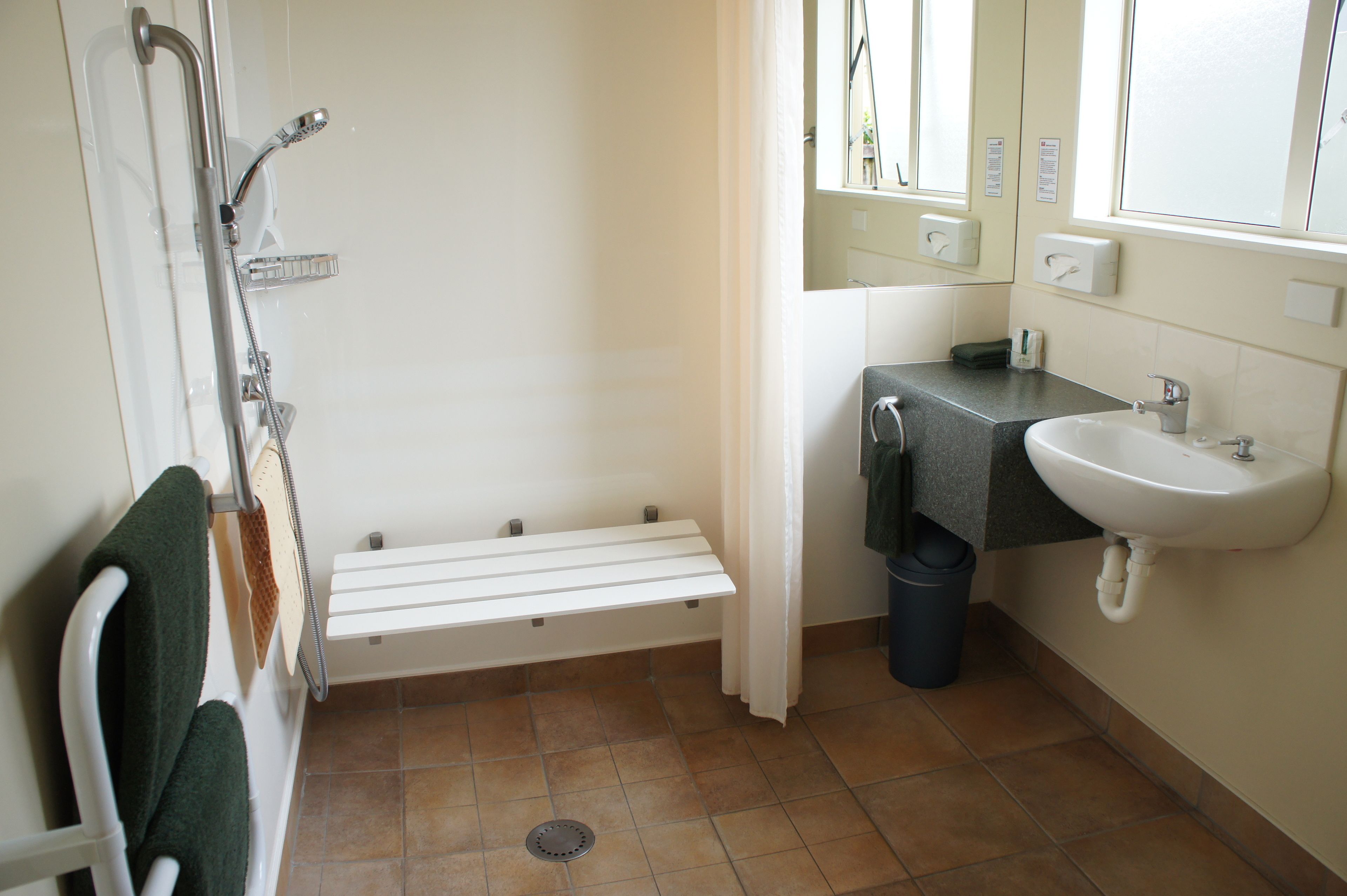 Un baño con ducha, lavamanos y una banca.