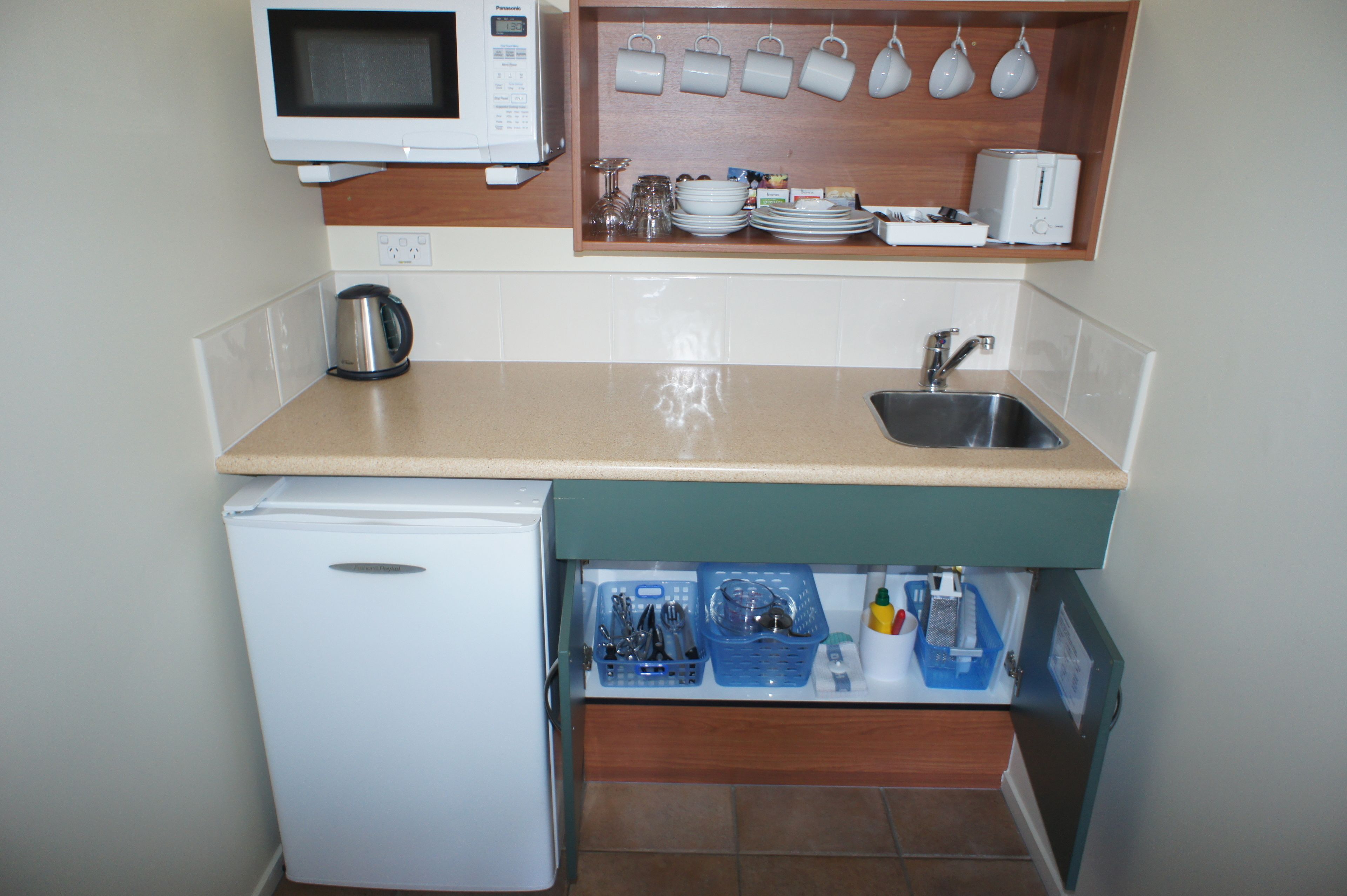 Una kitchenette compacta con microondas, pileta y espacio para guardar vajilla y utensilios.