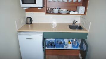 Una kitchenette compacta con microondas, pileta y espacio para guardar vajilla y utensilios.