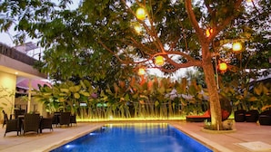 A pool area with a fountain, surrounded by chairs and tables, and illuminated by hanging lanterns.