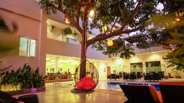 An indoor pool area with lounge chairs, a tree, and a seating area with tables and chairs.