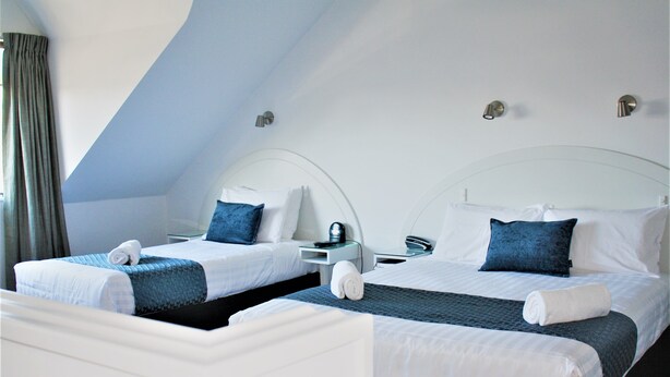 Dos camas individuales con ropa de cama blanca y azul, una mesita de noche y una lámpara de pared.