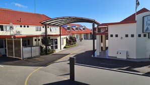 Entrada de un hotel con un paseo techado, un cartel que dice 'Brougham Heights Motel' y un camino de entrada con puerta de reja.