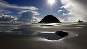 Una playa con una gran formación rocosa, agua tranquila y cielo despejado.