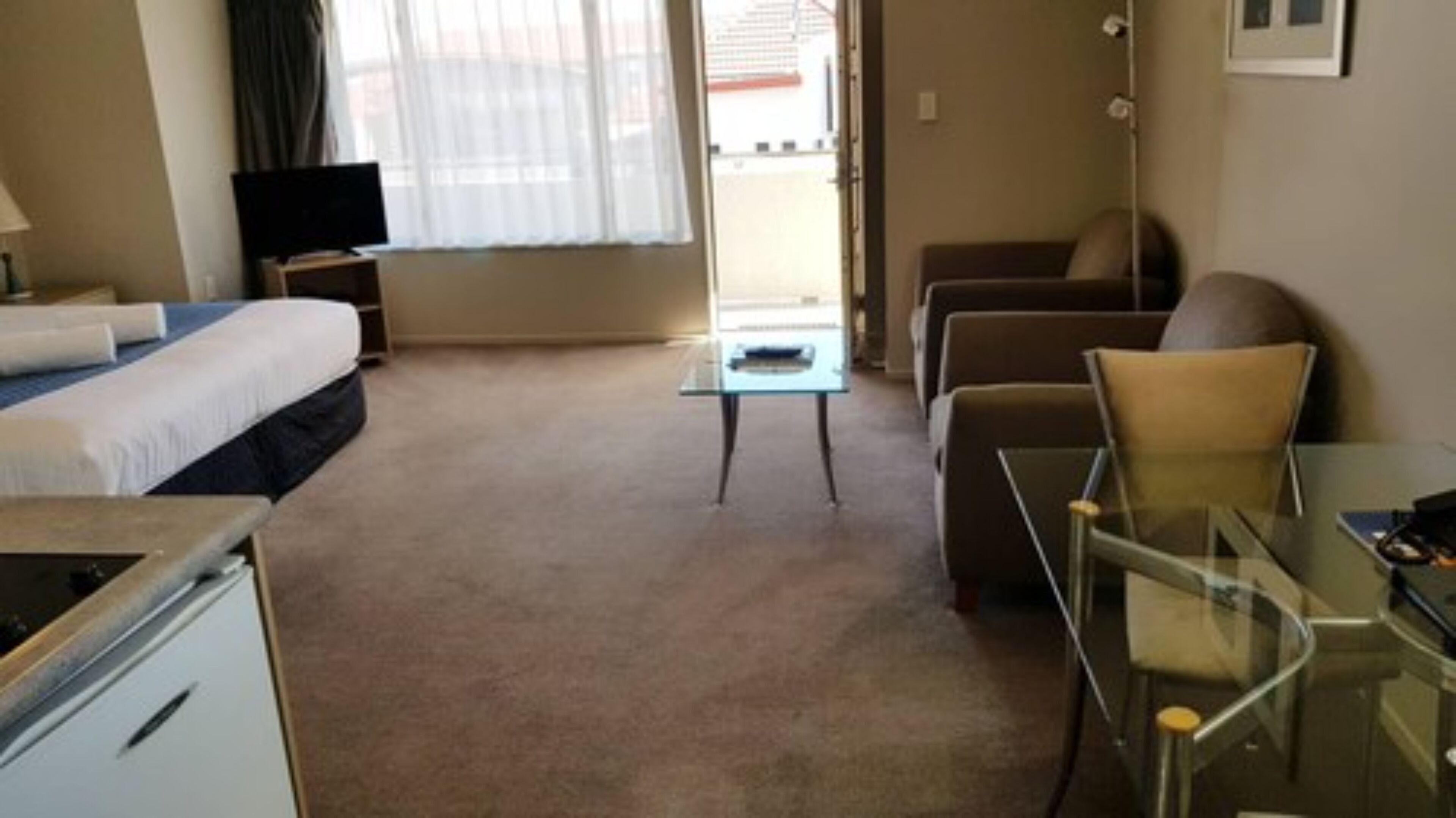 A hotel room with a bed, a desk, a chair, a small table, and a television.