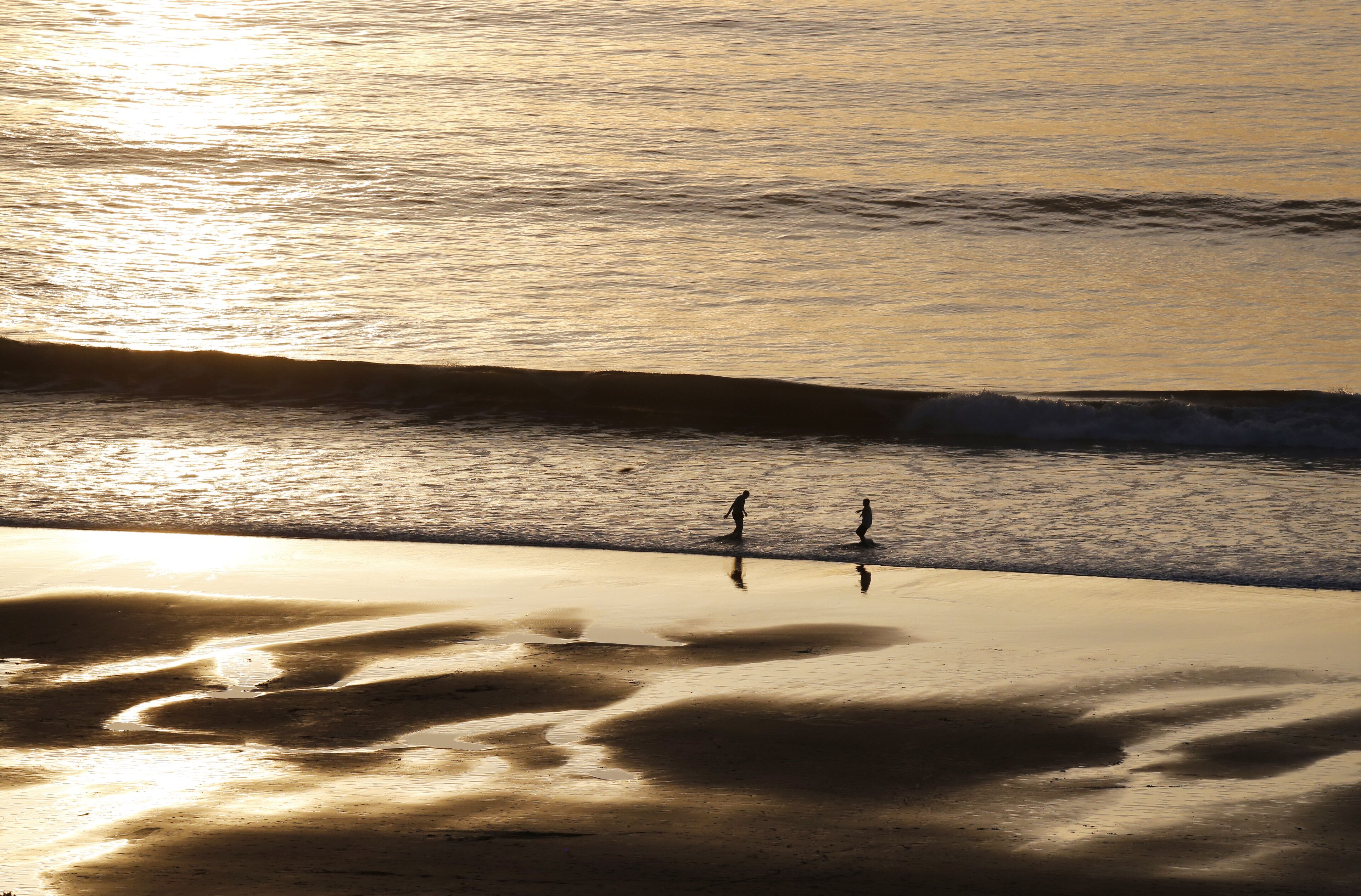 Escena de playa con dos personas caminando por la orilla.
