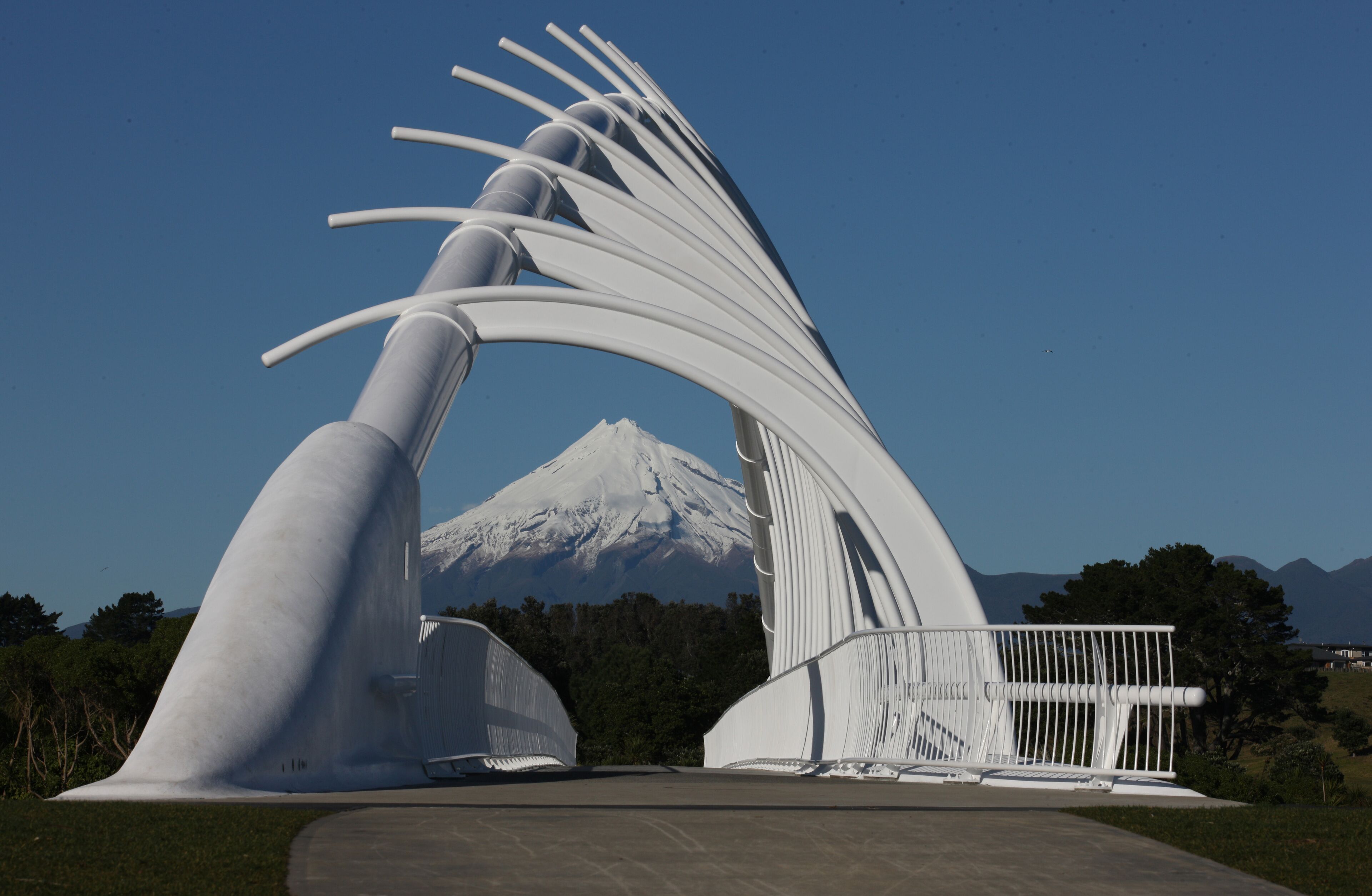 Una gran escultura blanca con diseño curvo, frente a un paisaje de montaña nevada y cielo azul despejado.