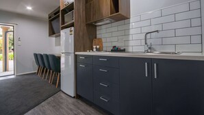 Una cocina moderna con armarios oscuros, encimera blanca y horno empotrado. En la zona de comedor contigua hay sillas y una pequeña mesa.