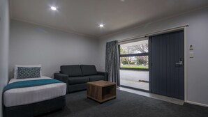 Una habitación de hotel moderna con una cama, un sofá, una pequeña mesa de madera y un ventanal corredero que da a un balcón.
