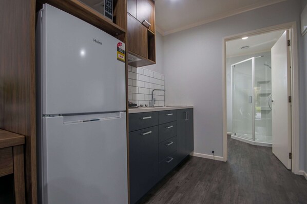 A modern kitchen with a white refrigerator, dark cabinets, and a tiled backsplash. - Antonio Mews Motel (Stratford)