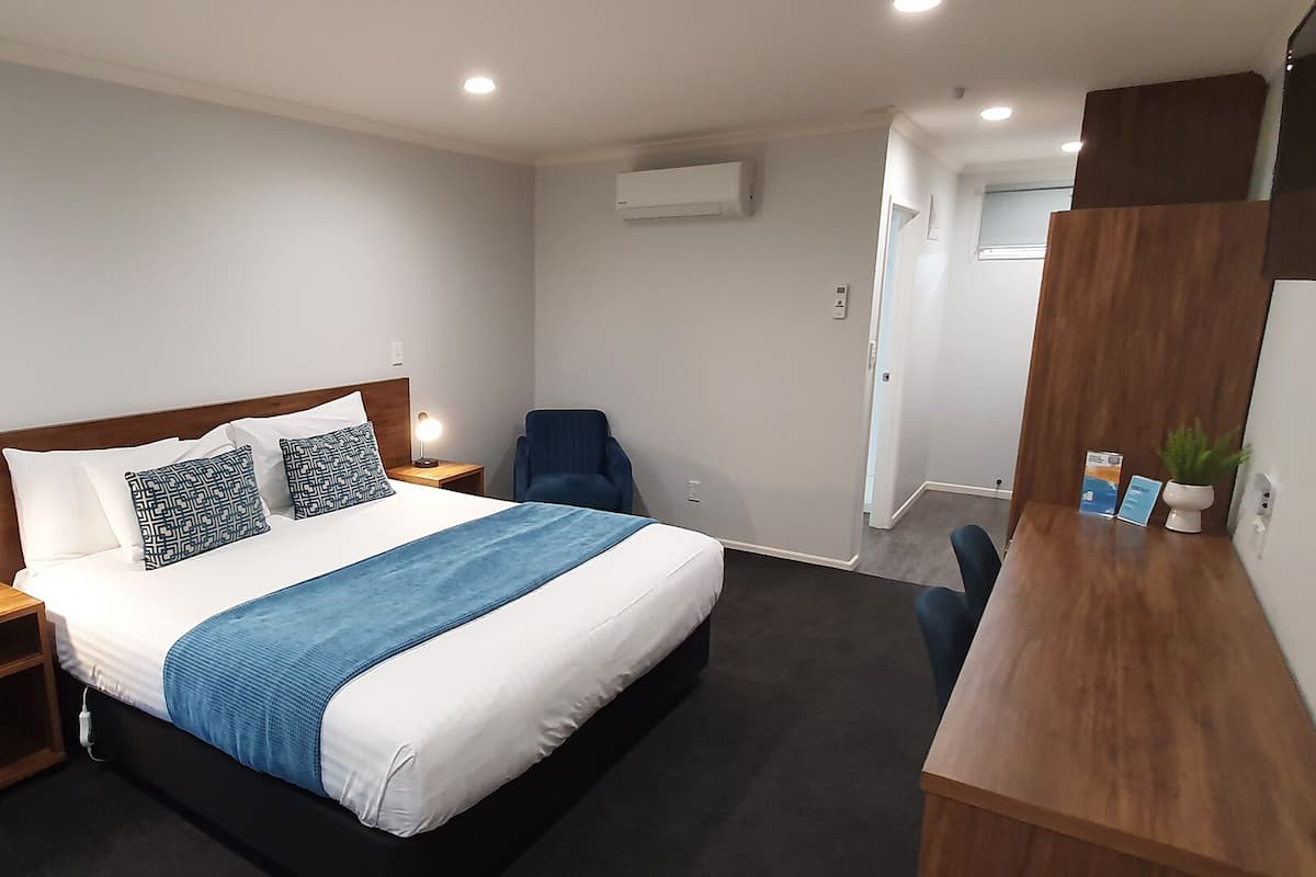 Een hotelkamer met een bed, nachtkastjes, een bureau, een stoel en een airconditioning.