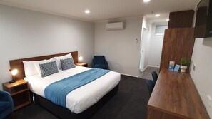 A hotel room with a bed, bedside tables, a desk, a chair, and an air conditioning unit. - Antonio Mews Motel (Stratford)