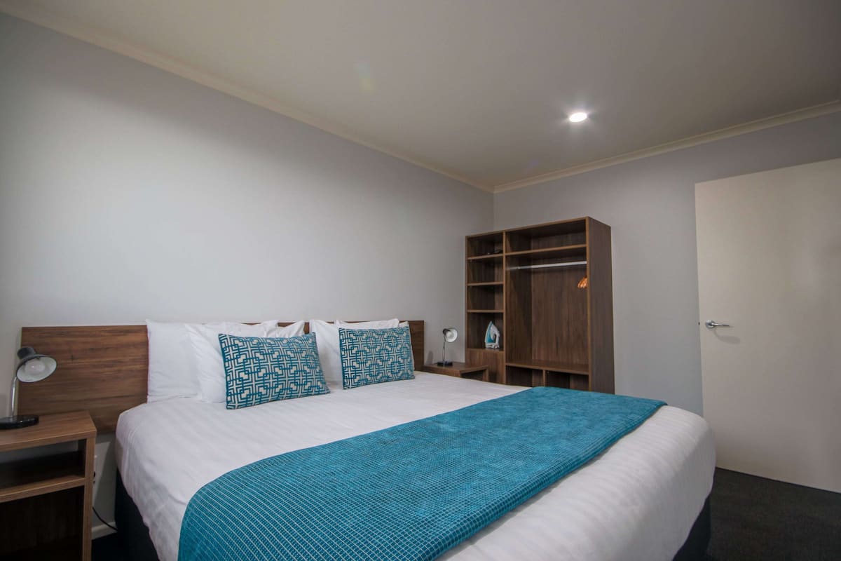 Een slaapkamer met een groot bed, een nachtkastje, een kledingkast en een deur.