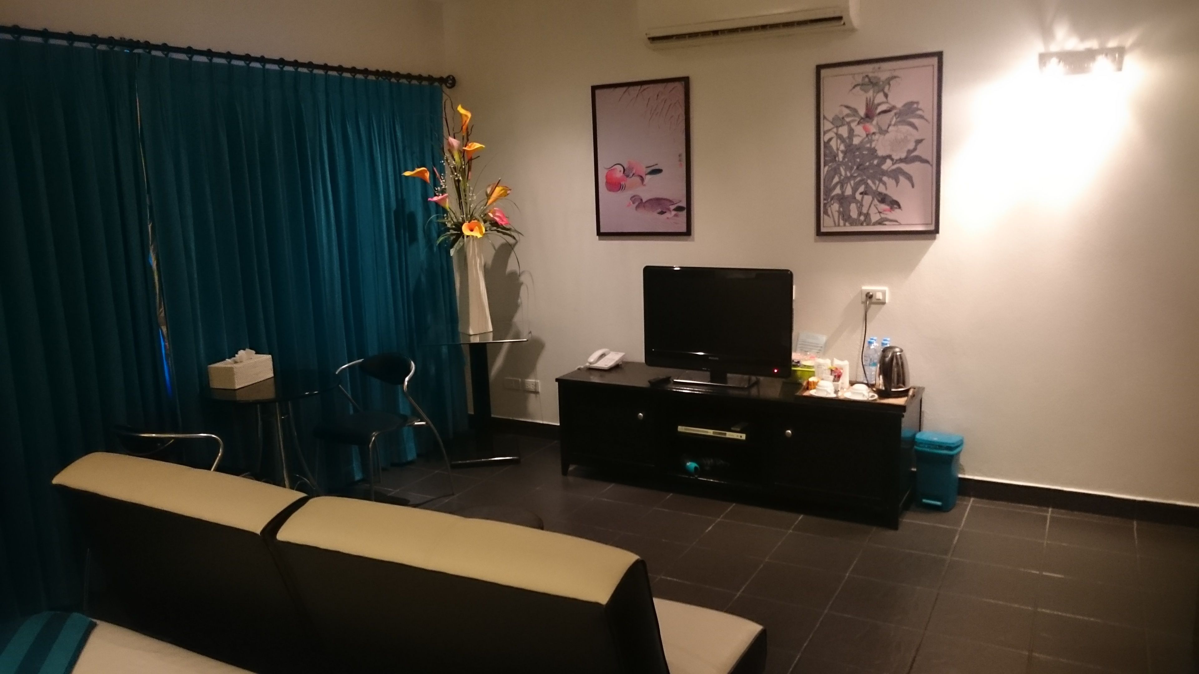 Une chambre d’hôtel équipée d’un téléviseur à écran plat, d’un bureau avec un téléphone, d’un vase avec des fleurs et de deux tableaux encadrés accrochés au mur.