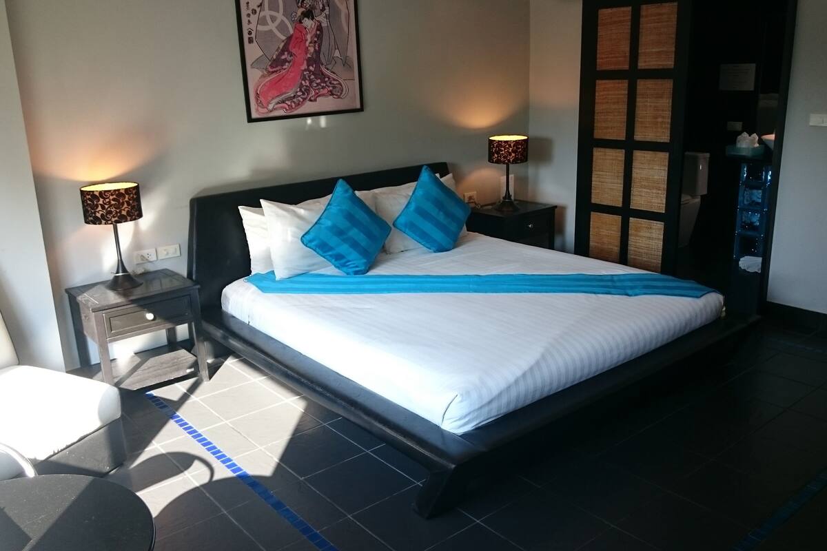 Habitación de hotel con una cama grande, dos mesitas de noche, una silla y un cuadro en la pared.
