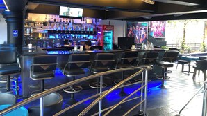 Eine Bar mit einer Theke, Barhocker und einem Fernseher, der eine Sendung zeigt.