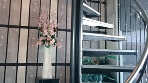 Eine Wendeltreppe mit Metallgeländer, eine dekorative Leuchte darüber und eine Vase mit Blumen auf einem kleinen Tisch daneben.