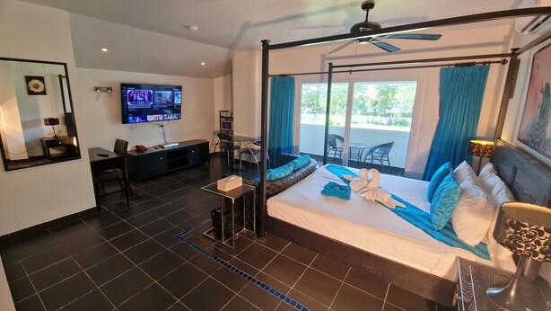 Ein modernes Hotelzimmer mit einem großen Bett, einem Fernseher, einem Balkon mit Sitzgelegenheiten und einem Deckenventilator.