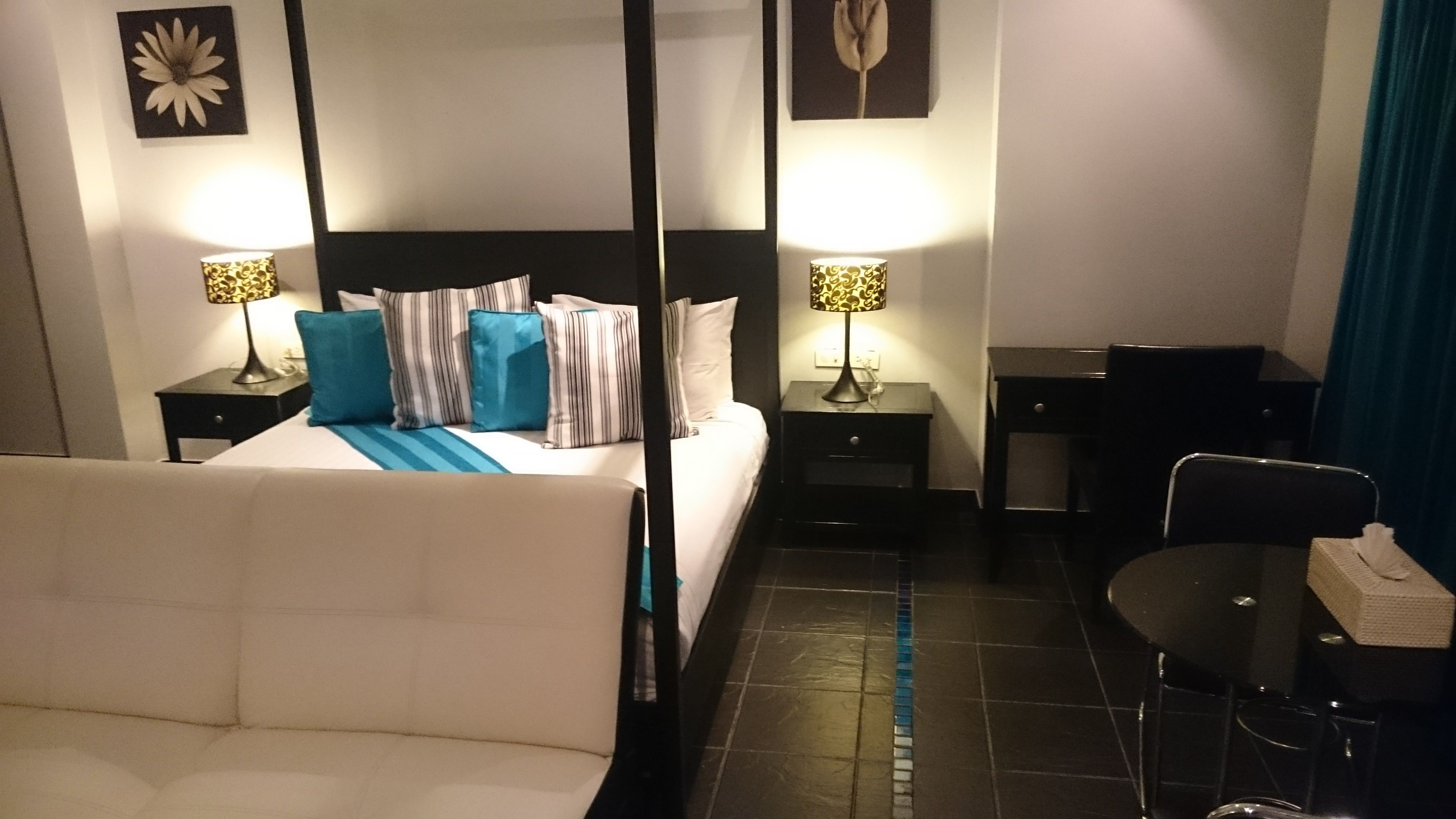 Habitación de hotel con cama con dosel, dos mesitas de noche con lámparas, un escritorio con silla y un gran ventanal con vistas.
