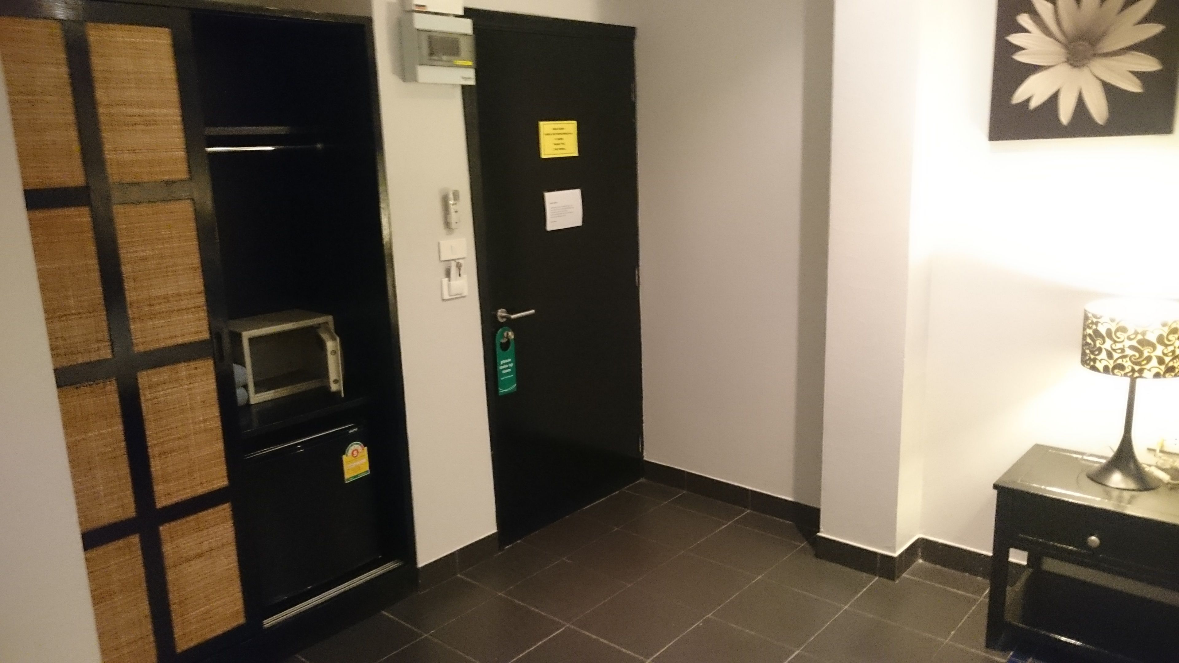Hotelkamer met een zwarte deur, een magnetron, een klein tafeltje met een lamp en een bloemdecoratie aan de muur.