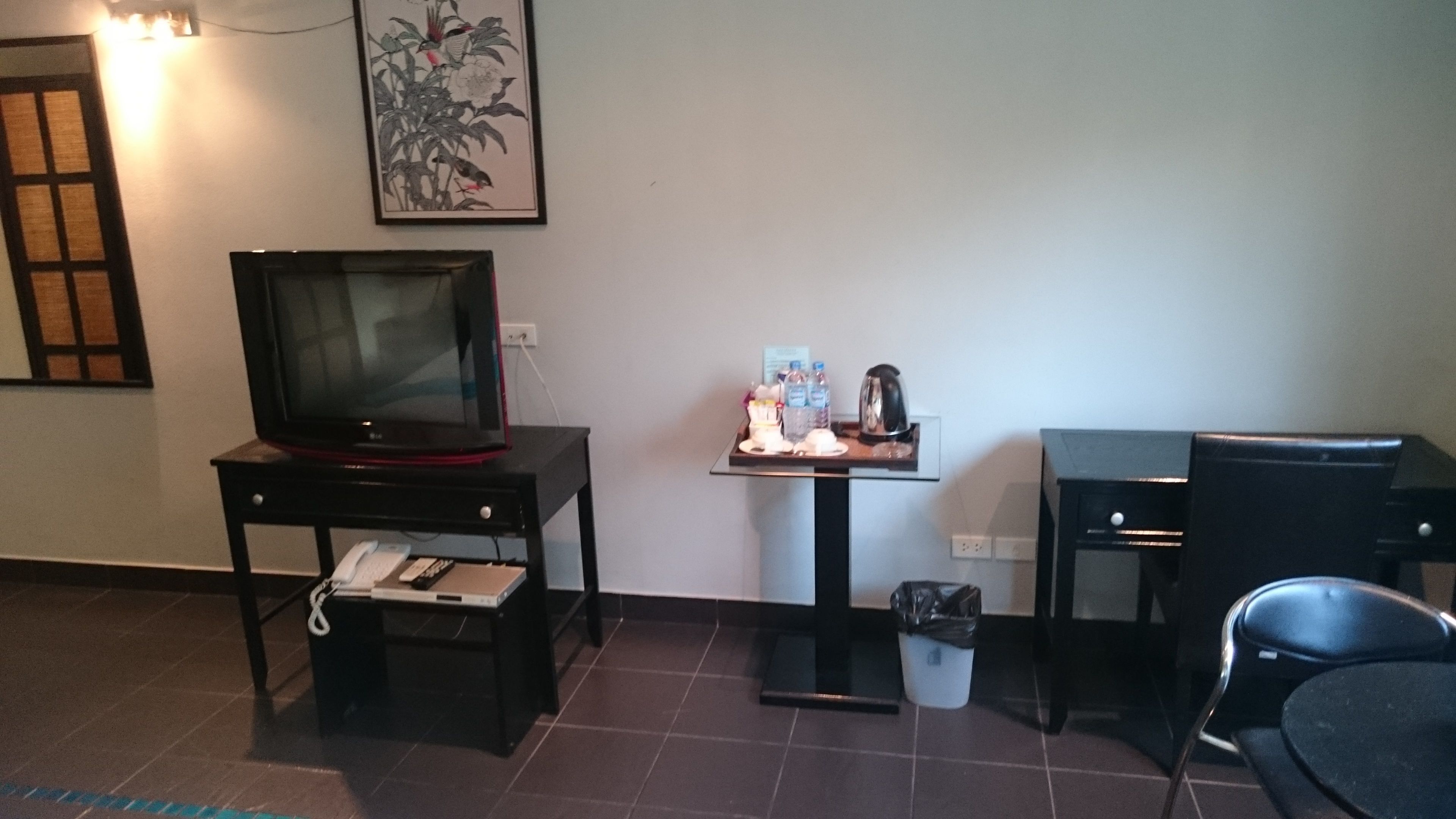 A hotel room with a television on a stand, a small table with a tray of items, a trash bin, and a chair.
