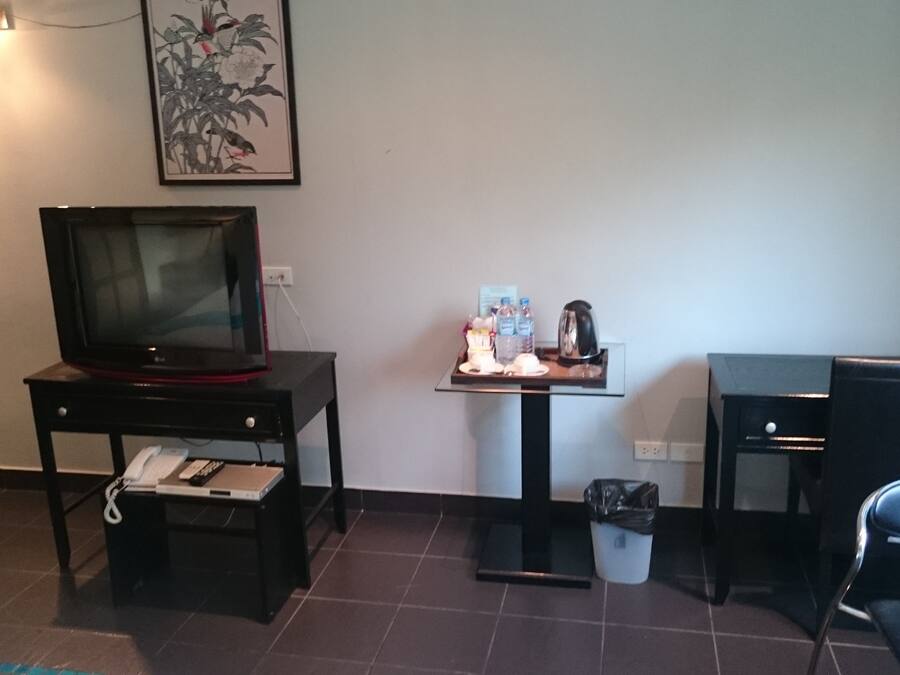 A hotel room with a television on a stand, a small table with a tray of items, a trash bin, and a chair.