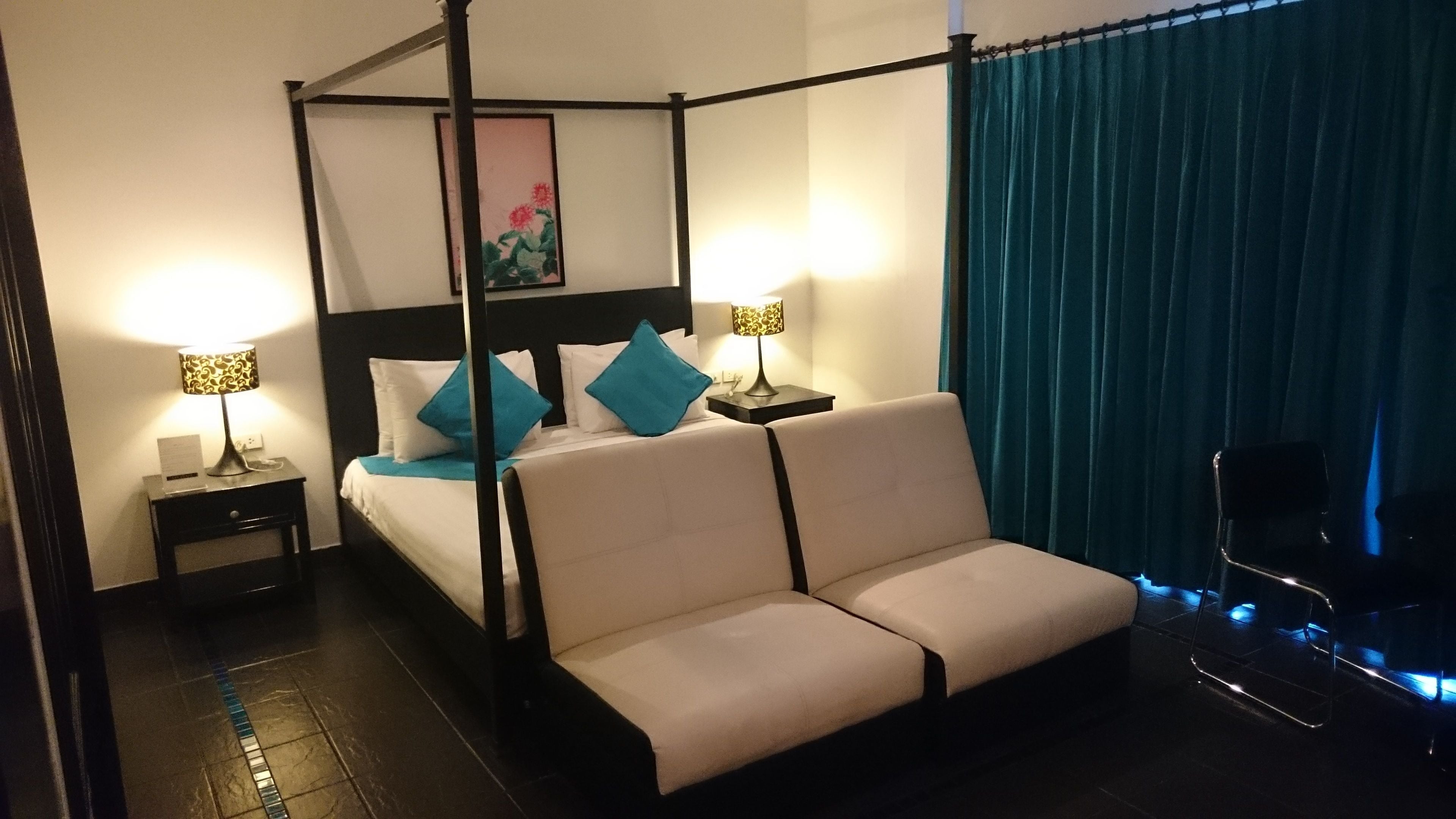 Ein Bett mit Himmelbett, ein Kopfteil, zwei Nachttische mit Lampen, ein Sofa und ein Sessel.