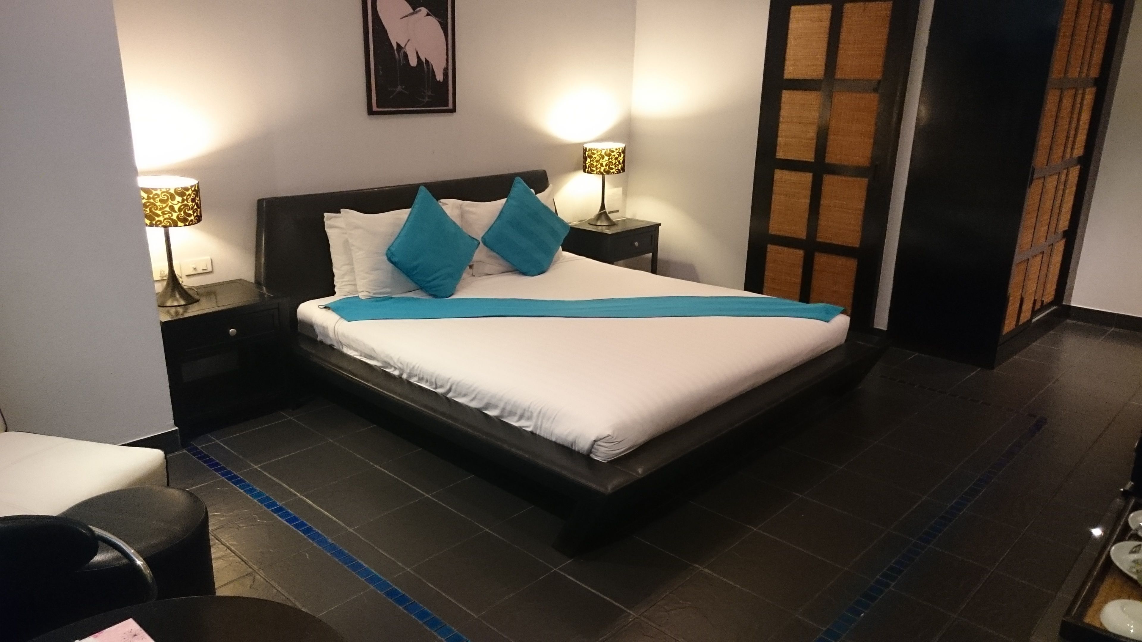 A neatly made bed with white and blue bedding, two bedside lamps, and a framed artwork on the wall.
