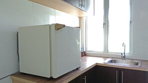 Une cuisine avec un réfrigérateur blanc, un plan de travail en bois, des meubles de rangement sombres et une fenêtre avec un évier.