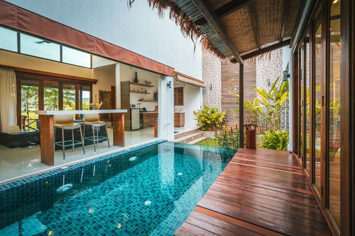 A modern outdoor swimming pool with a wooden deck, a bar area, and a view of the surrounding landscape.