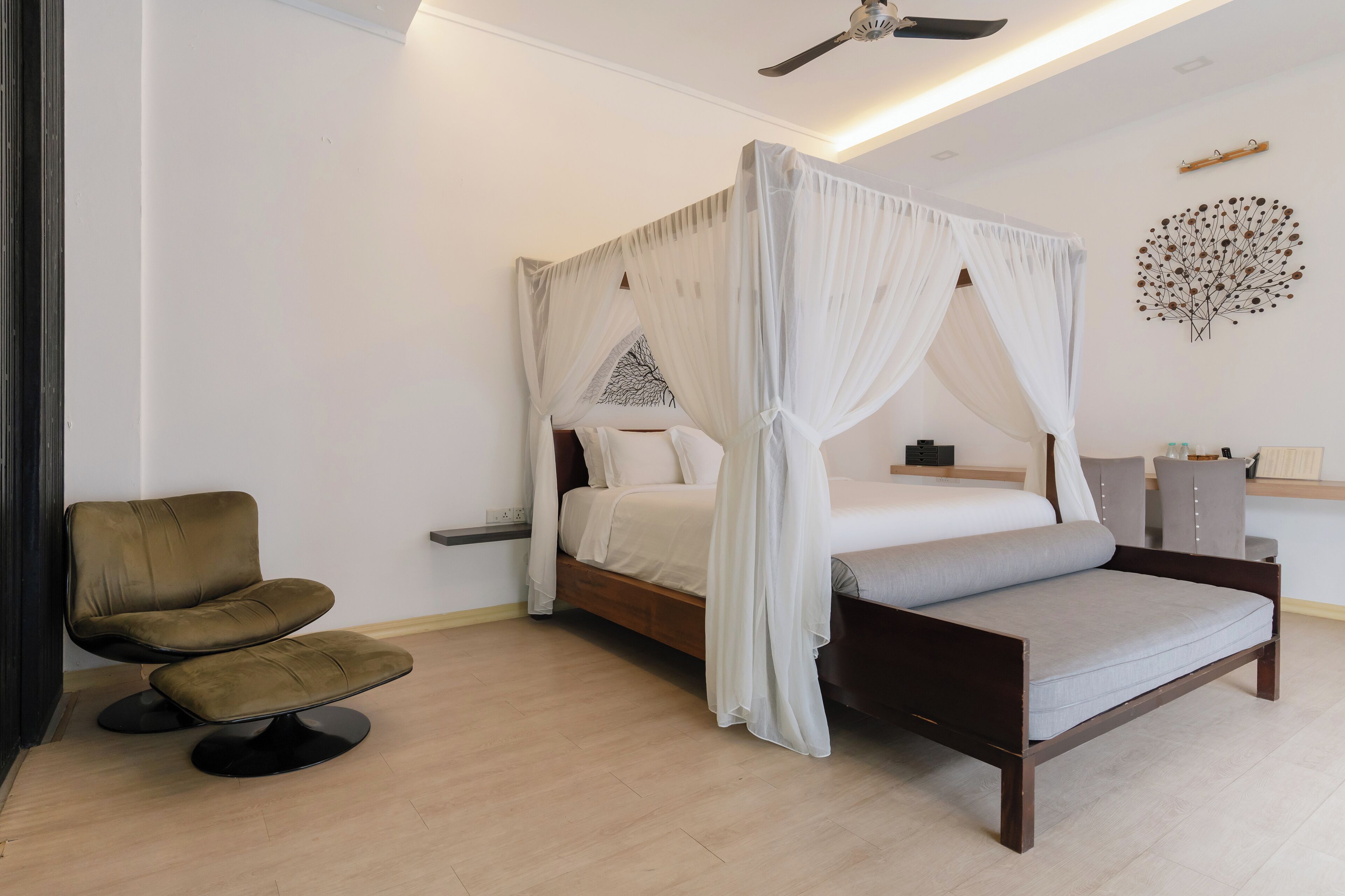A bedroom with a four-poster bed, a bedside table, a chair, and a ceiling fan.