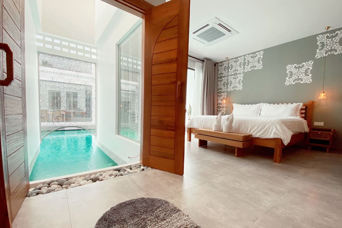 A bedroom with a bed, a view of a pool, and a wooden door leading to a balcony.