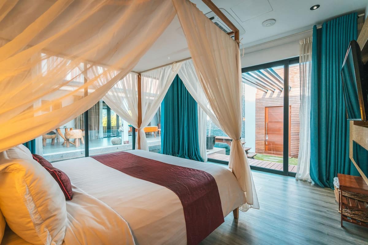 A bedroom with a canopy bed, large windows, and a view of the outside.