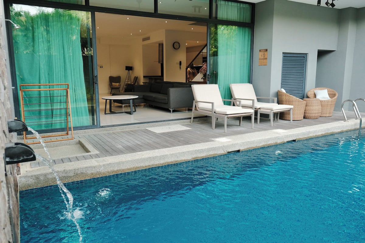 A modern indoor pool area with a clear view of the adjacent living space, including a sofa and a dining table.