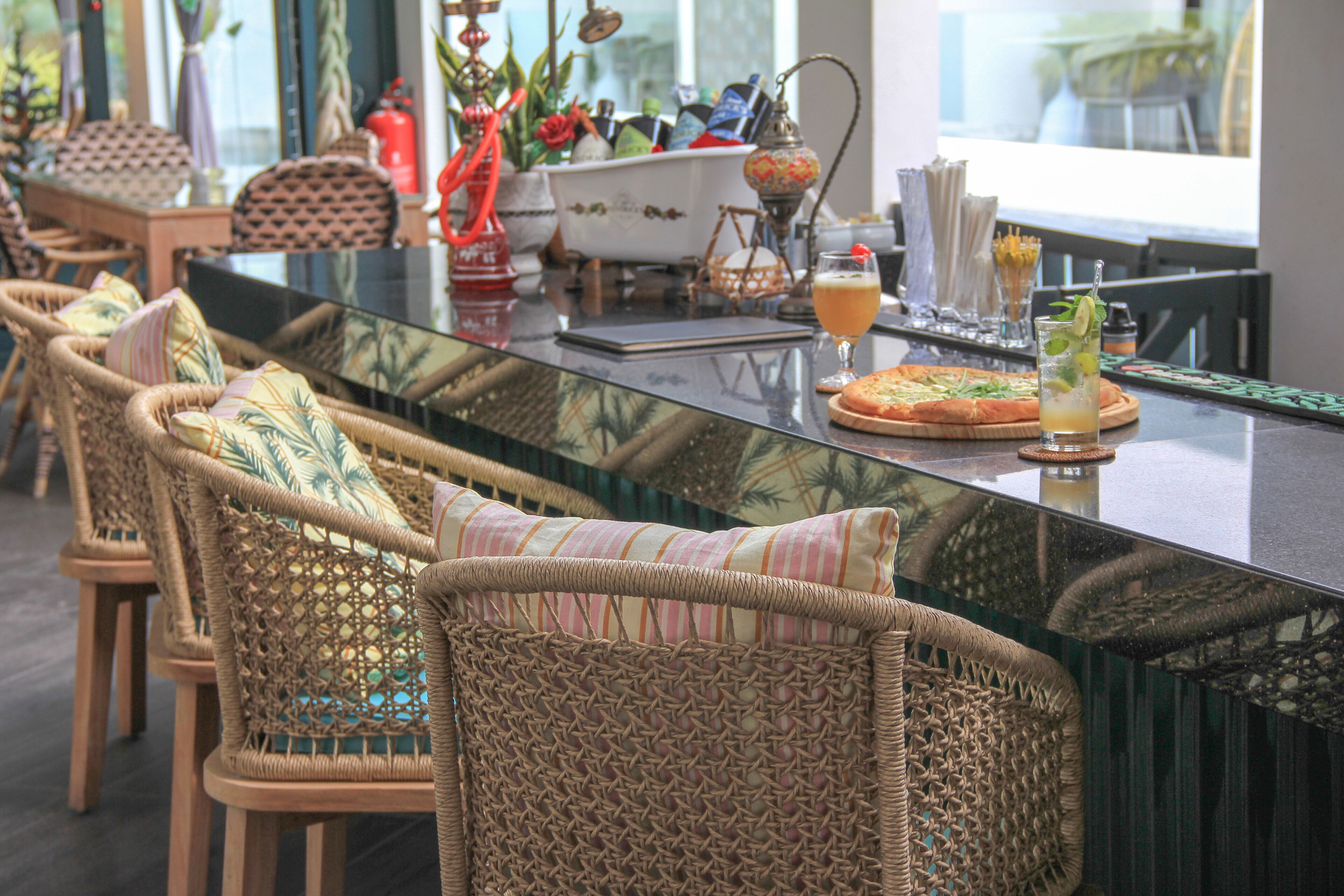 A restaurant with wicker chairs, a glass-top table, and a pizza.