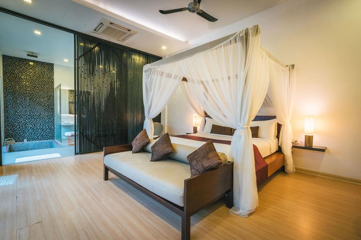A modern bedroom with a bed, bedside tables, and a view of a pool.