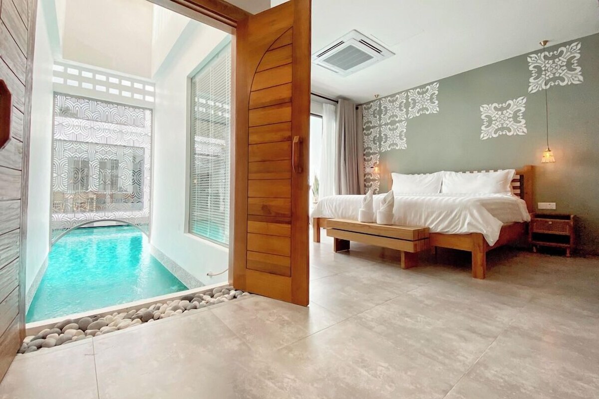 A bedroom with a bed, bedside tables, a nightstand, a window, and a view of a swimming pool.