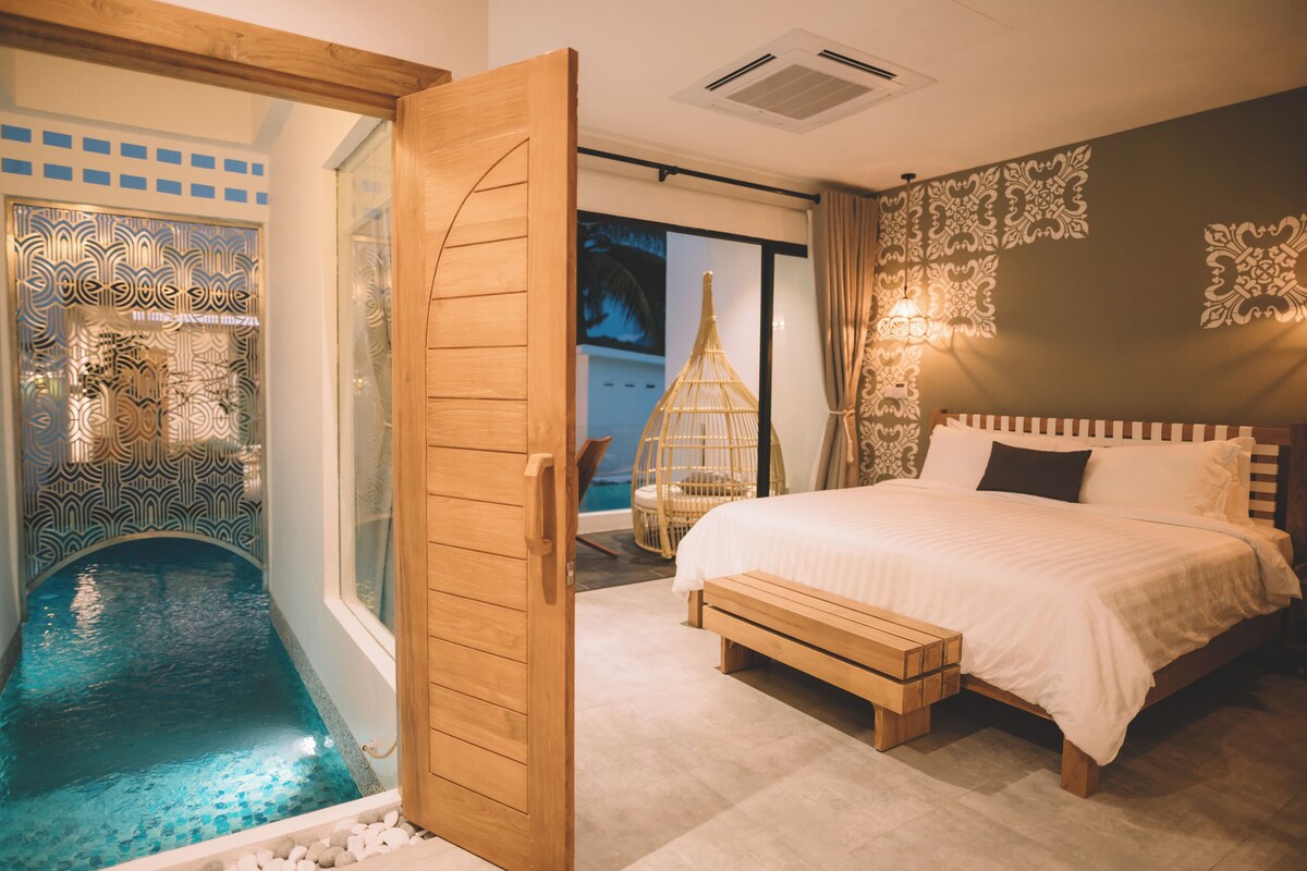 A bedroom with a large bed, a small wooden bench, a decorative wall, and a glass door leading to a pool area.